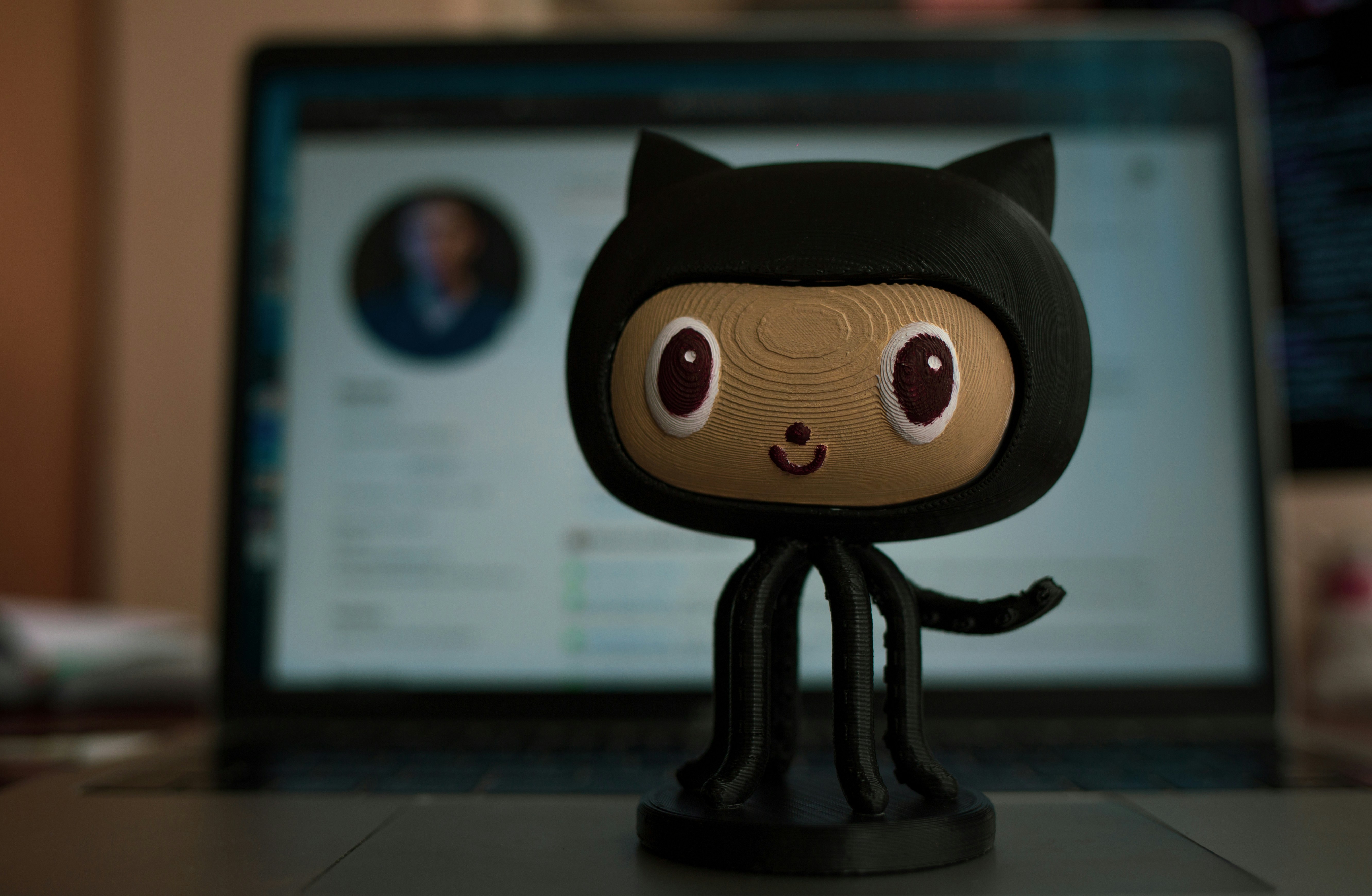 A picture of a 3D-printed version of Github's Octocat, in front of a computer screen